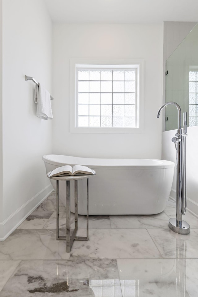 full bath featuring marble finish floor, baseboards, and a freestanding tub