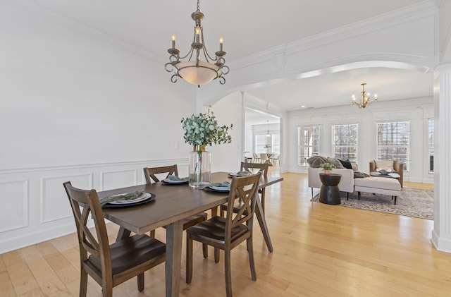 dining area featuring an inviting chandelier, arched walkways, ornamental molding, light wood-style floors, and a decorative wall