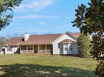 view of front of house featuring covered porch, a chimney, and a front lawn