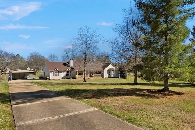 view of front facade featuring an outbuilding, concrete driveway, a front yard, a carport, and a chimney