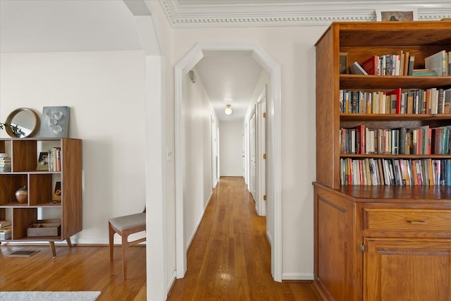 corridor featuring light wood-style flooring, arched walkways, and baseboards