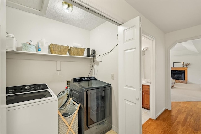 clothes washing area with washer and dryer, light wood-style floors, a fireplace, baseboards, and laundry area