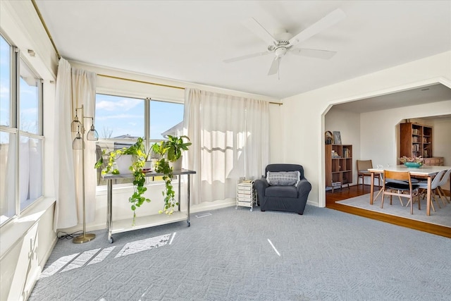 living area featuring arched walkways, a ceiling fan, and carpet flooring