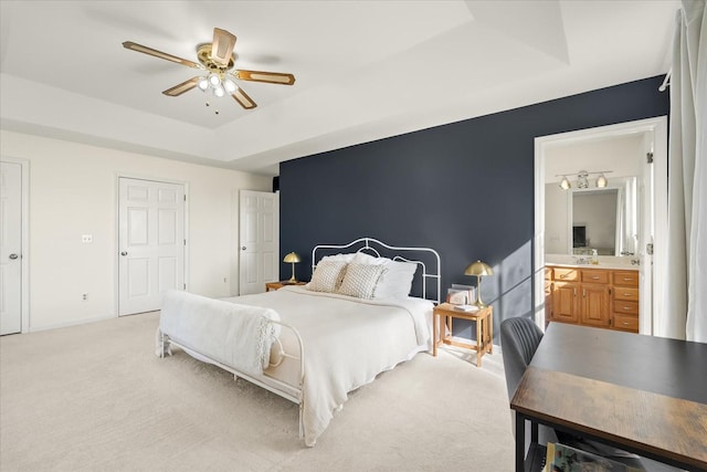 bedroom featuring baseboards, ensuite bath, a sink, light carpet, and a raised ceiling