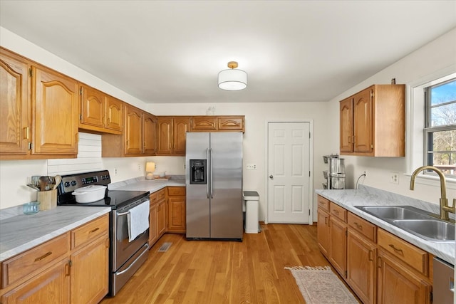 kitchen featuring appliances with stainless steel finishes, light countertops, light wood-style floors, and a sink