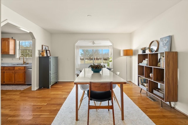 dining space featuring baseboards, arched walkways, and light wood finished floors