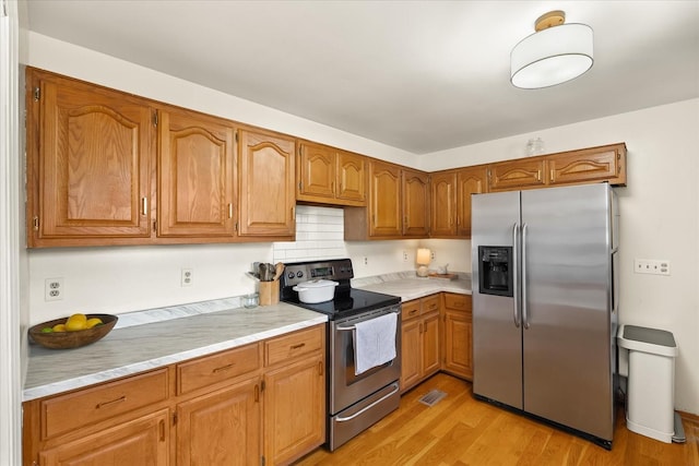 kitchen with light countertops, brown cabinetry, light wood-style floors, and appliances with stainless steel finishes