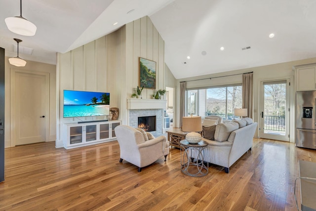 living room with visible vents, high vaulted ceiling, a warm lit fireplace, and light wood finished floors