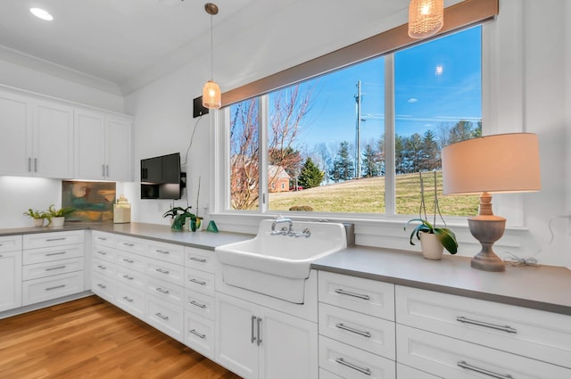 kitchen featuring pendant lighting, white cabinetry, light wood-style floors, and a sink