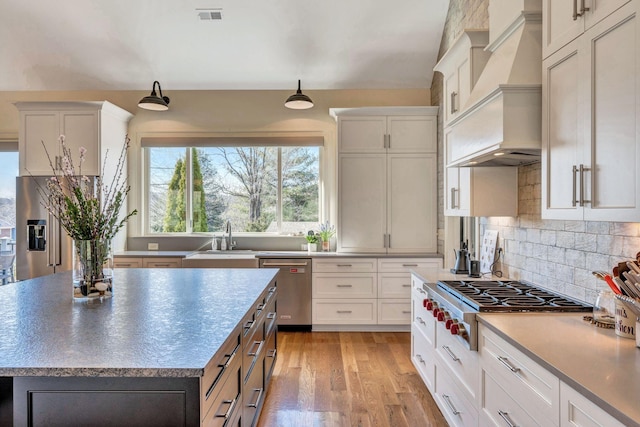 kitchen with visible vents, custom range hood, a sink, light wood-style floors, and appliances with stainless steel finishes