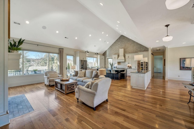 living room featuring light wood-type flooring, visible vents, baseboards, and high vaulted ceiling