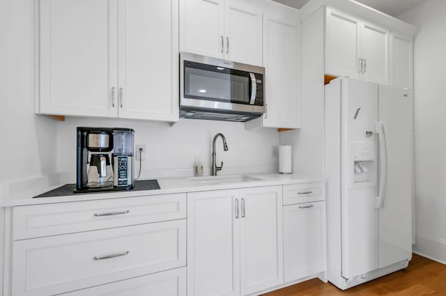 kitchen featuring a sink, stainless steel microwave, white fridge with ice dispenser, white cabinets, and light countertops