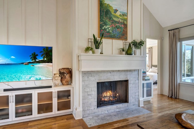 living area with wood finished floors, a fireplace, and vaulted ceiling