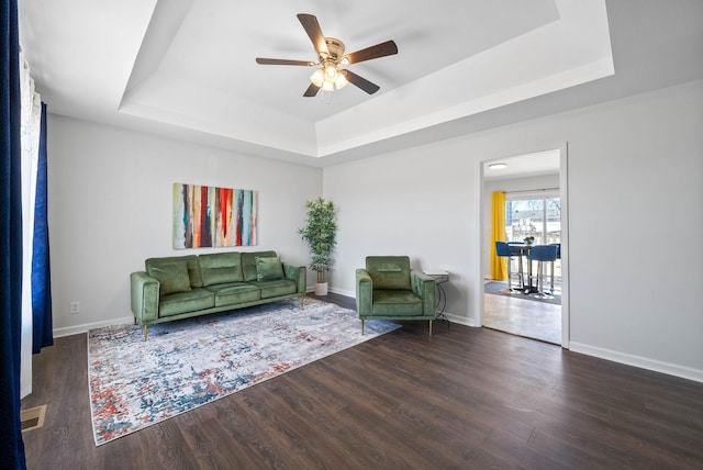 unfurnished living room featuring a tray ceiling, wood finished floors, baseboards, and ceiling fan