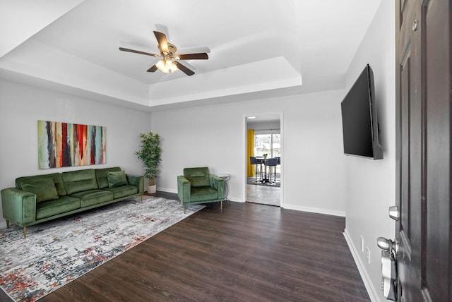 living room featuring dark wood-style floors, ceiling fan, baseboards, and a tray ceiling