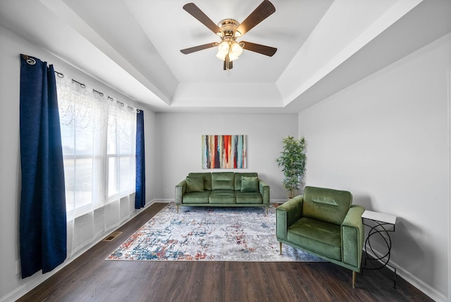 sitting room with a ceiling fan, wood finished floors, visible vents, baseboards, and a raised ceiling