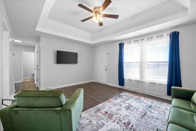 living area with ceiling fan, baseboards, a tray ceiling, and wood finished floors