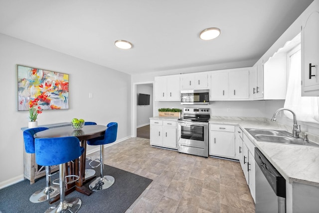 kitchen featuring baseboards, a sink, light countertops, appliances with stainless steel finishes, and white cabinetry