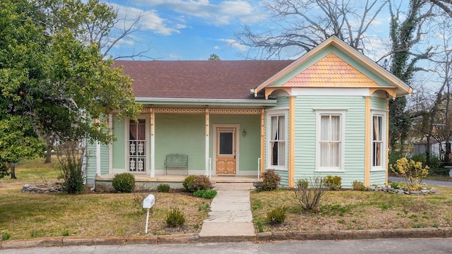 victorian-style house with a porch, a front yard, and a shingled roof