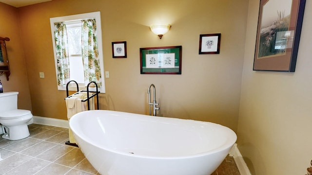 bathroom with tile patterned flooring, toilet, baseboards, and a freestanding bath