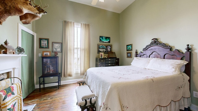 bedroom with wood finished floors, a fireplace, baseboards, ceiling fan, and vaulted ceiling