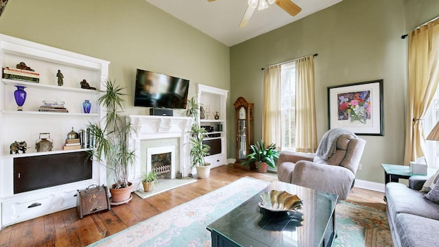 living area with a fireplace with raised hearth, baseboards, lofted ceiling, wood finished floors, and a ceiling fan