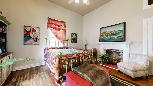 bedroom featuring baseboards, a fireplace with raised hearth, wood finished floors, and a ceiling fan