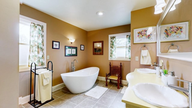 full bath with tile patterned flooring, a freestanding tub, baseboards, and a sink