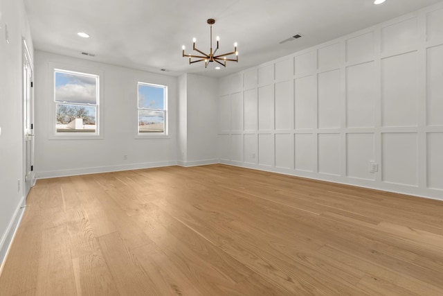 unfurnished room featuring an inviting chandelier, a decorative wall, light wood-style floors, and visible vents