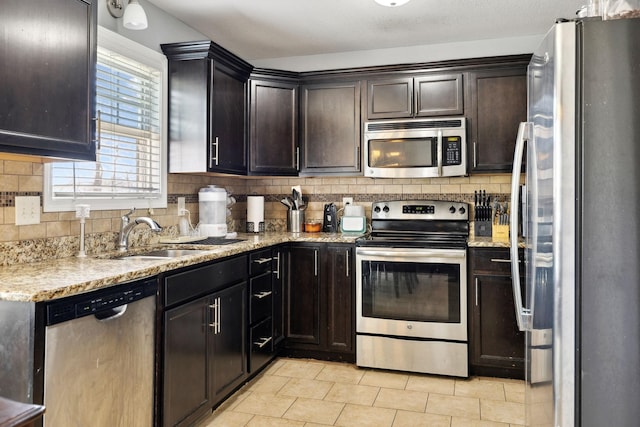 kitchen featuring backsplash, light stone countertops, stainless steel appliances, and a sink