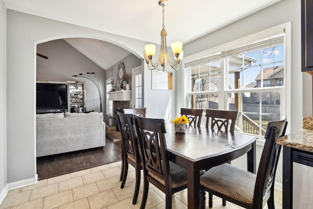 dining room featuring baseboards, lofted ceiling, a fireplace, arched walkways, and a chandelier