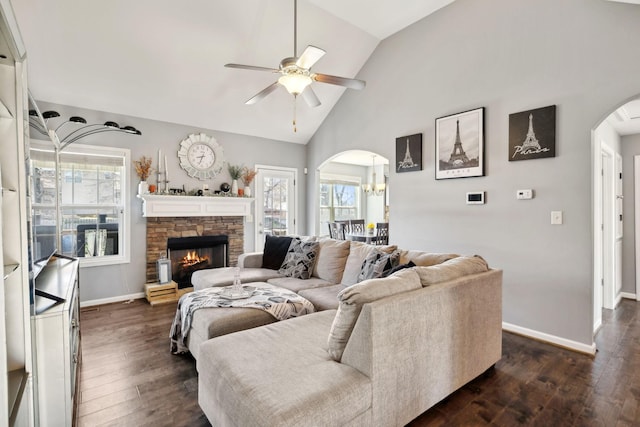 living room featuring arched walkways, a stone fireplace, dark wood-style floors, and a ceiling fan