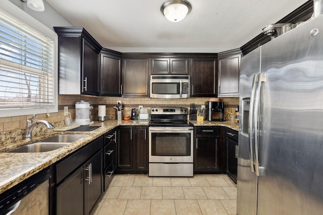 kitchen featuring backsplash, light stone counters, light tile patterned floors, appliances with stainless steel finishes, and a sink