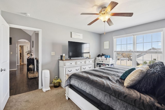 carpeted bedroom with a ceiling fan, arched walkways, and baseboards