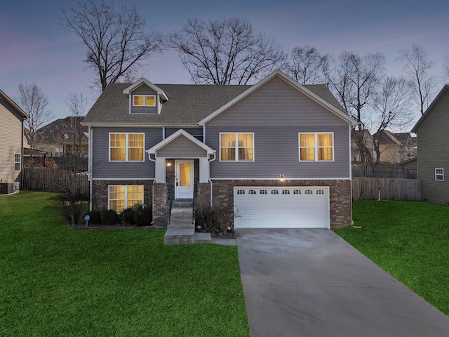 raised ranch featuring brick siding, an attached garage, fence, a lawn, and driveway