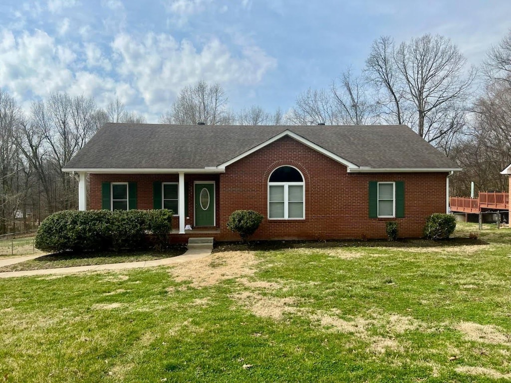 ranch-style home featuring brick siding, covered porch, a shingled roof, and a front lawn