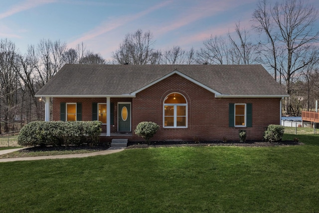 ranch-style house with a porch, a lawn, brick siding, and a shingled roof