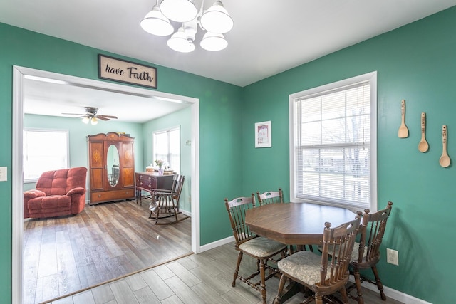 dining room with baseboards, wood finished floors, and ceiling fan with notable chandelier