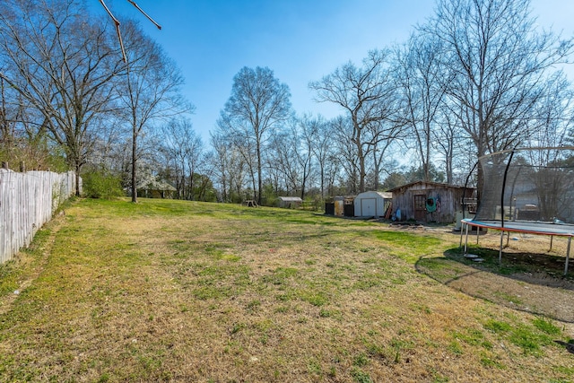 view of yard featuring an outbuilding, a storage shed, a trampoline, and fence