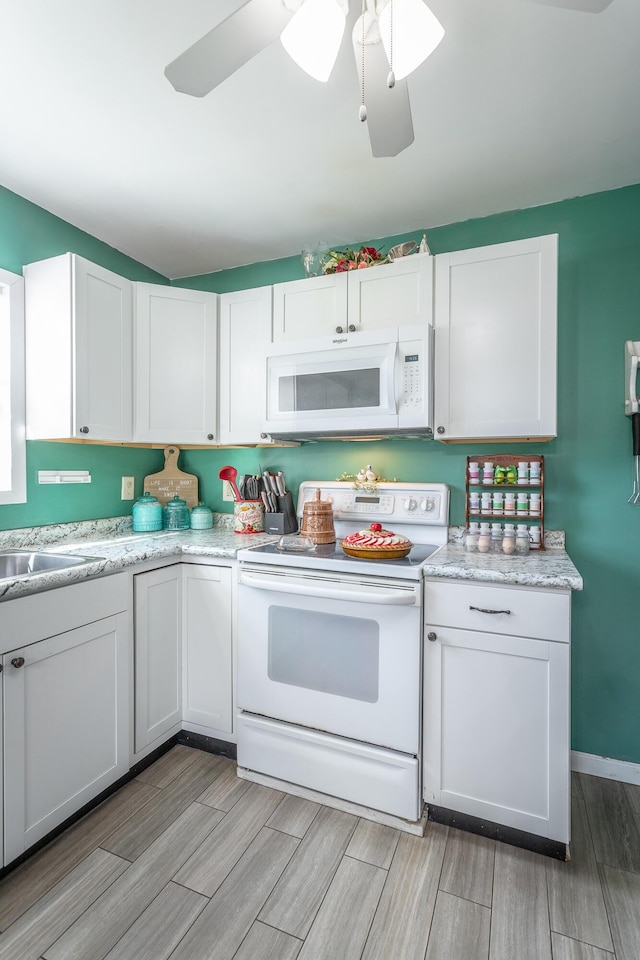 kitchen featuring wood finish floors, a sink, white cabinetry, white appliances, and ceiling fan