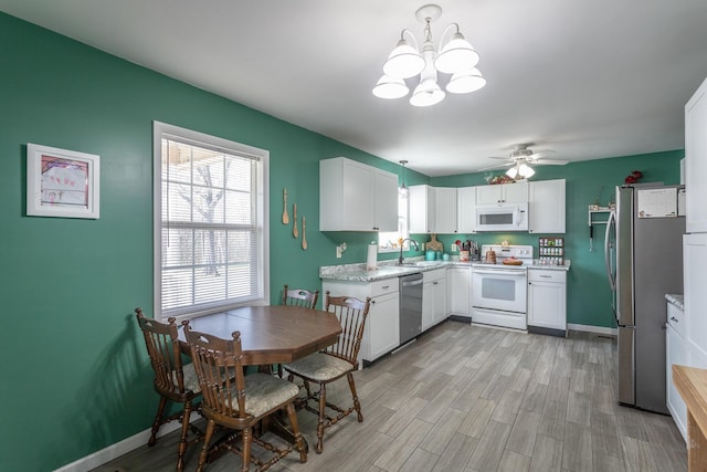 kitchen with a sink, white cabinetry, light wood-style floors, appliances with stainless steel finishes, and baseboards