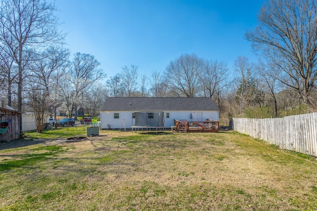 back of property with a trampoline, a lawn, a fenced backyard, and a wooden deck