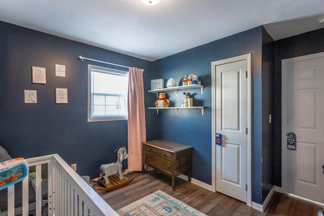 bedroom featuring a crib, baseboards, and wood finished floors