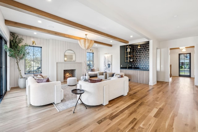 living area with light wood finished floors, beamed ceiling, indoor bar, and a lit fireplace