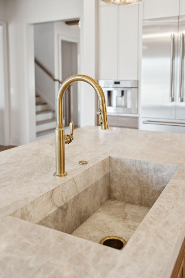 details featuring a sink, stainless steel built in refrigerator, white cabinets, and light countertops