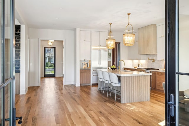 kitchen with light wood finished floors, light countertops, built in fridge, a kitchen bar, and tasteful backsplash