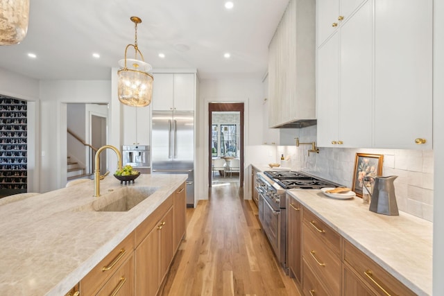 kitchen with backsplash, custom range hood, premium appliances, light wood-style floors, and a sink