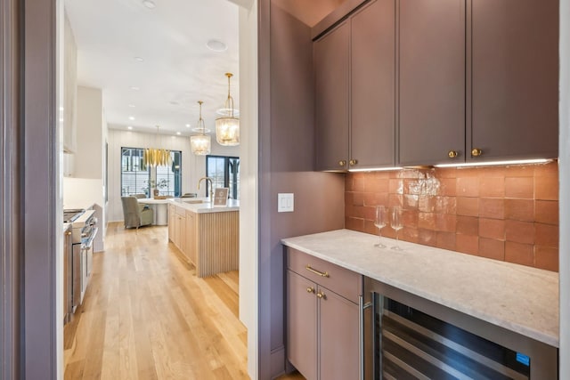 bar with light wood finished floors, wine cooler, decorative light fixtures, decorative backsplash, and a bar