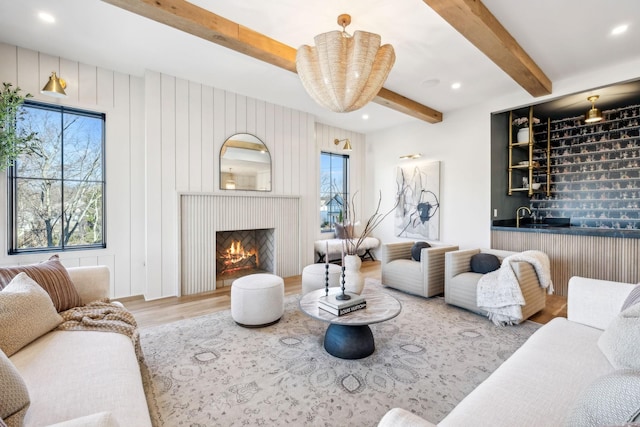 living room with beamed ceiling, plenty of natural light, a lit fireplace, and wood finished floors