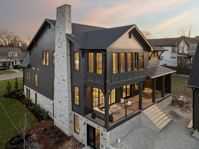 back of property at dusk with a patio, a lawn, roof with shingles, and a chimney